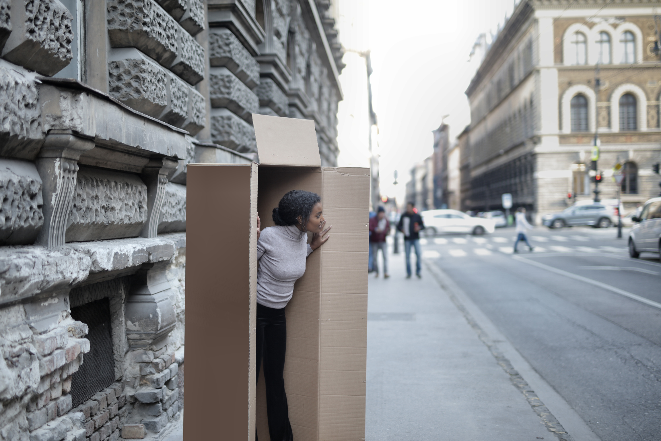 African American woman peeking out of cardboard box on sidewalk